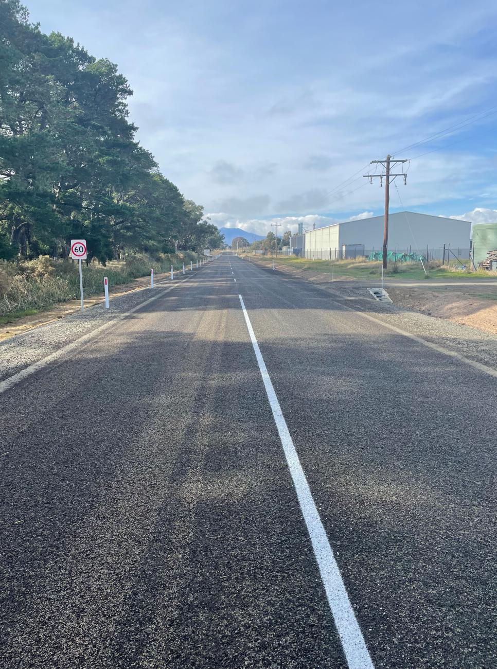 Long shot of a newly-sealed rural road, with trees alongside the roadway's edge