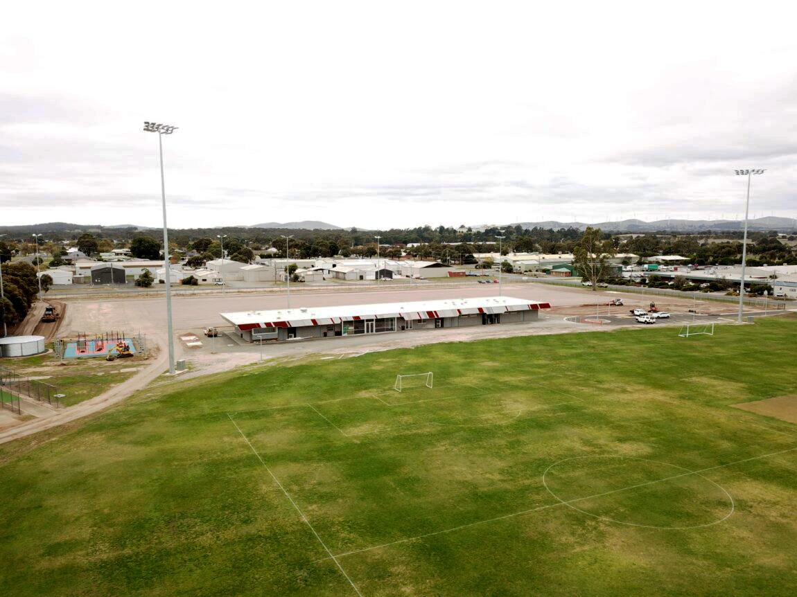 Long shot of a sporting pavilion with stadium lights, and large section of a grassy AFL playing field