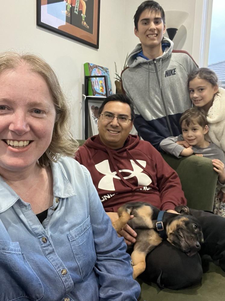 A family of five sitting on their couch and smiling, with a black puppy lying in the father's lap