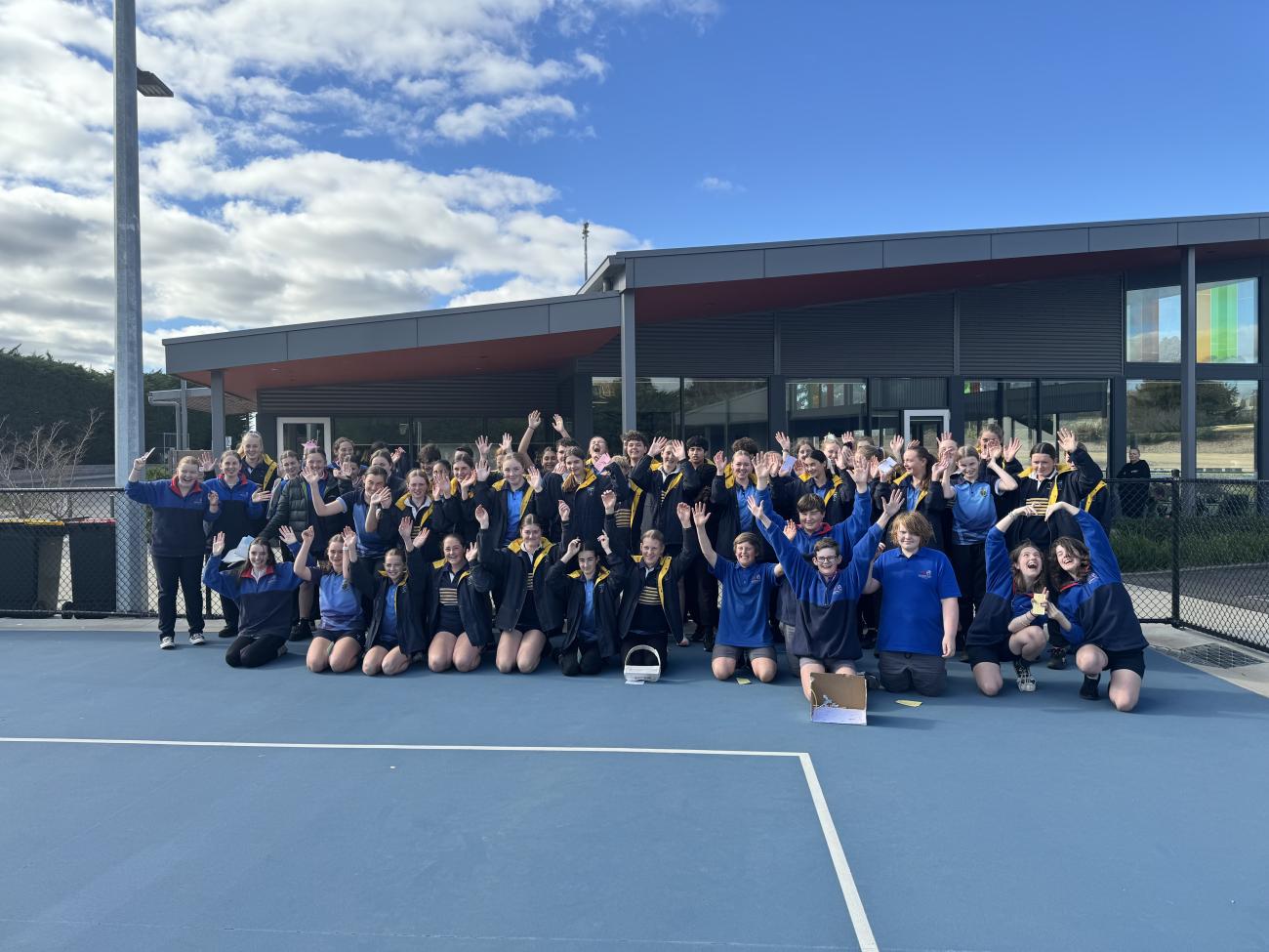 A group of 70 high school students outdoors, waving their hands in the air and smiling