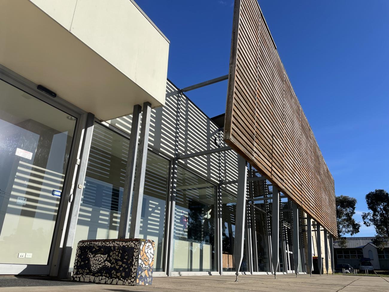 An attractive modern building surrounded by green grass, with a mosaic art piece in the entry walkway