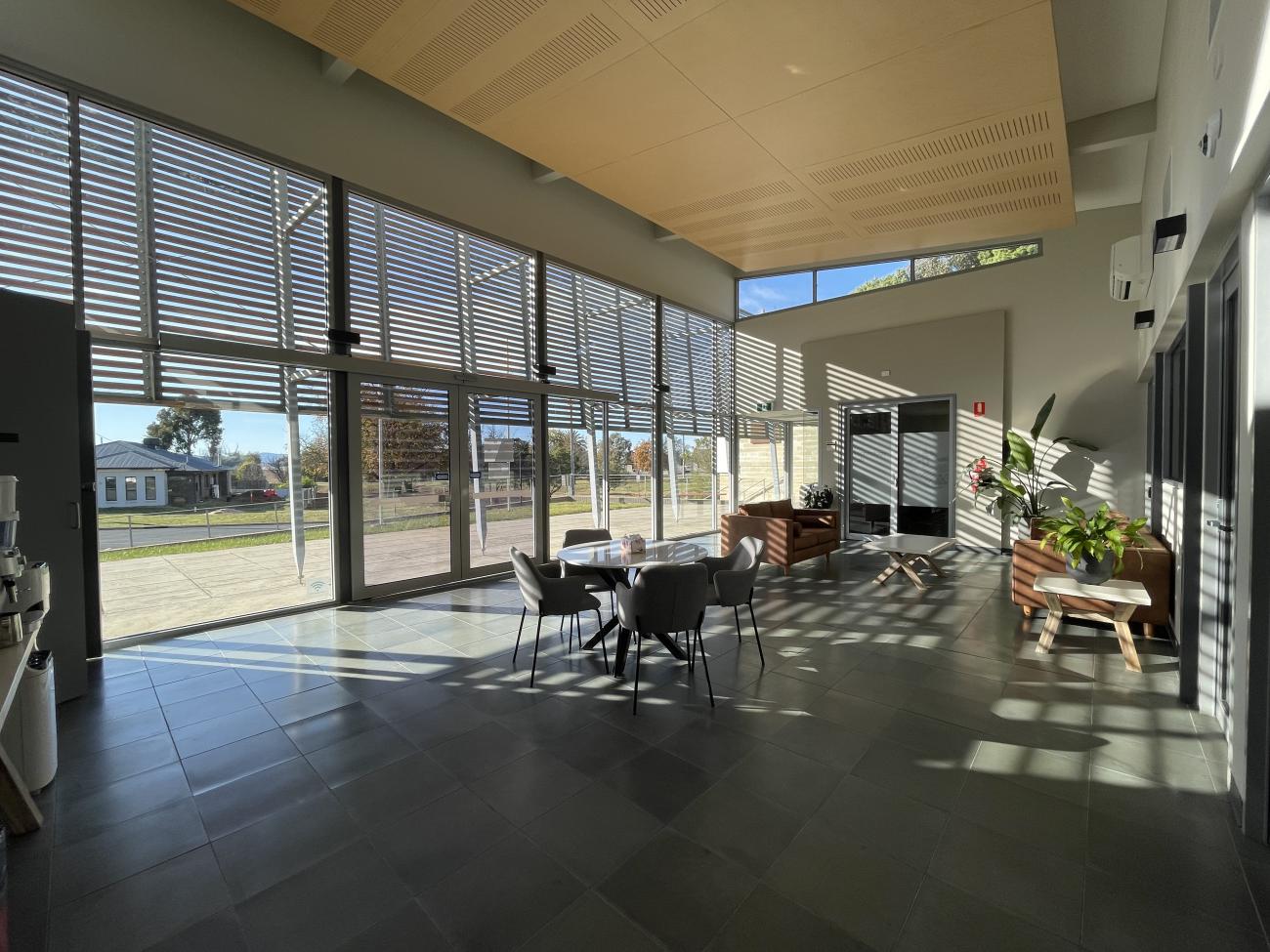 Interior lobby of a building, with indoor plants, sunlight and cafe-style seating