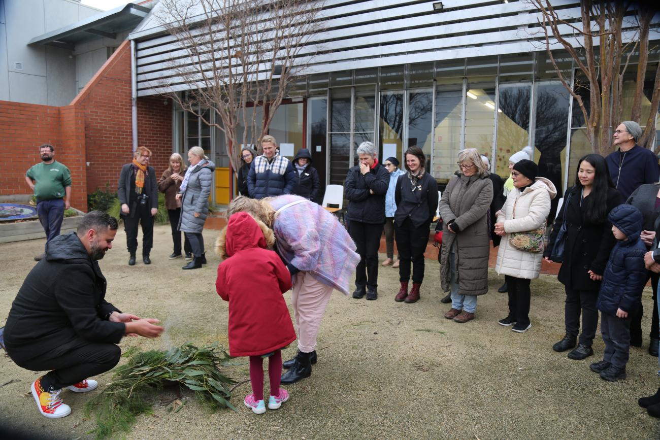 A young girl standing next to a fire with her mother at an Indigenous smoking ceremony