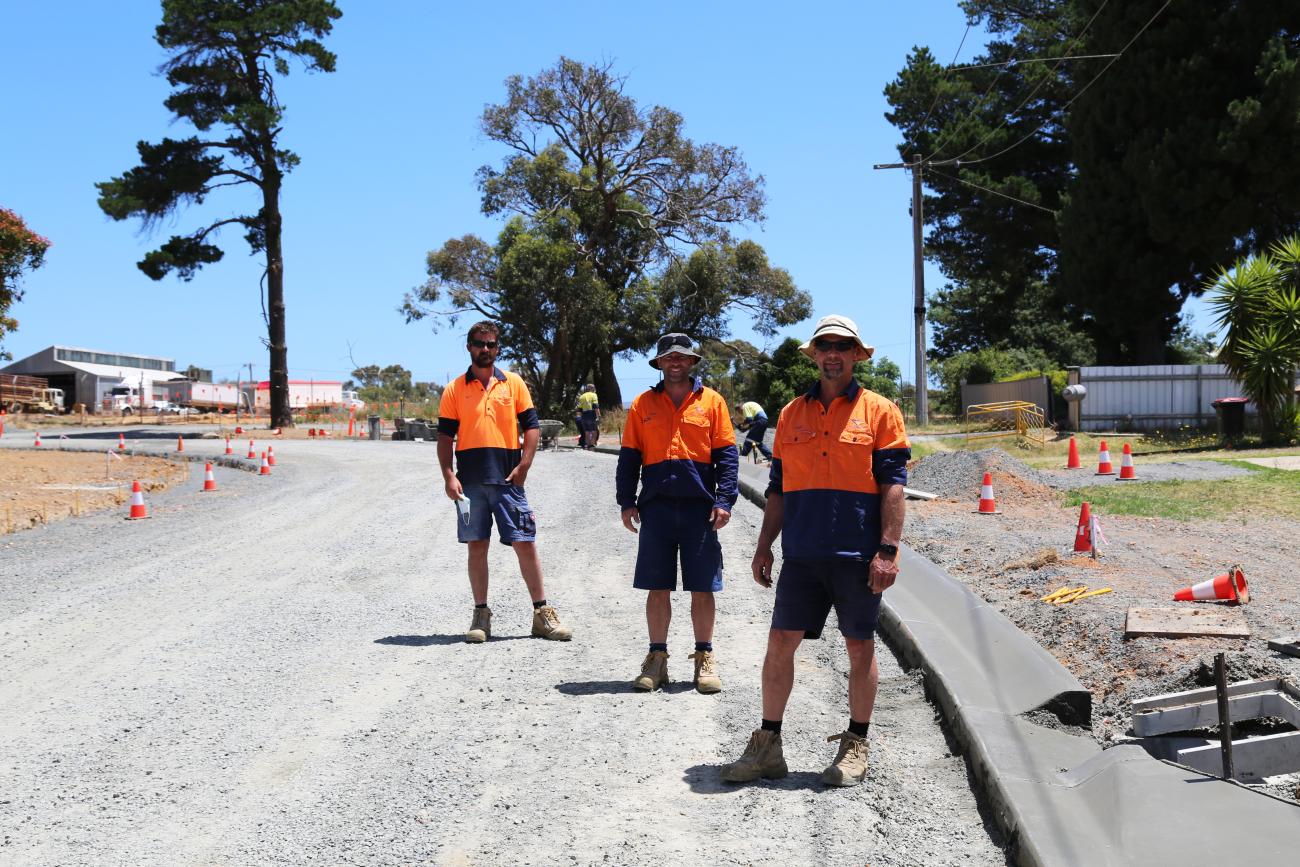 Three road workers in hi-viz standing on a sunny road and smiling at camera