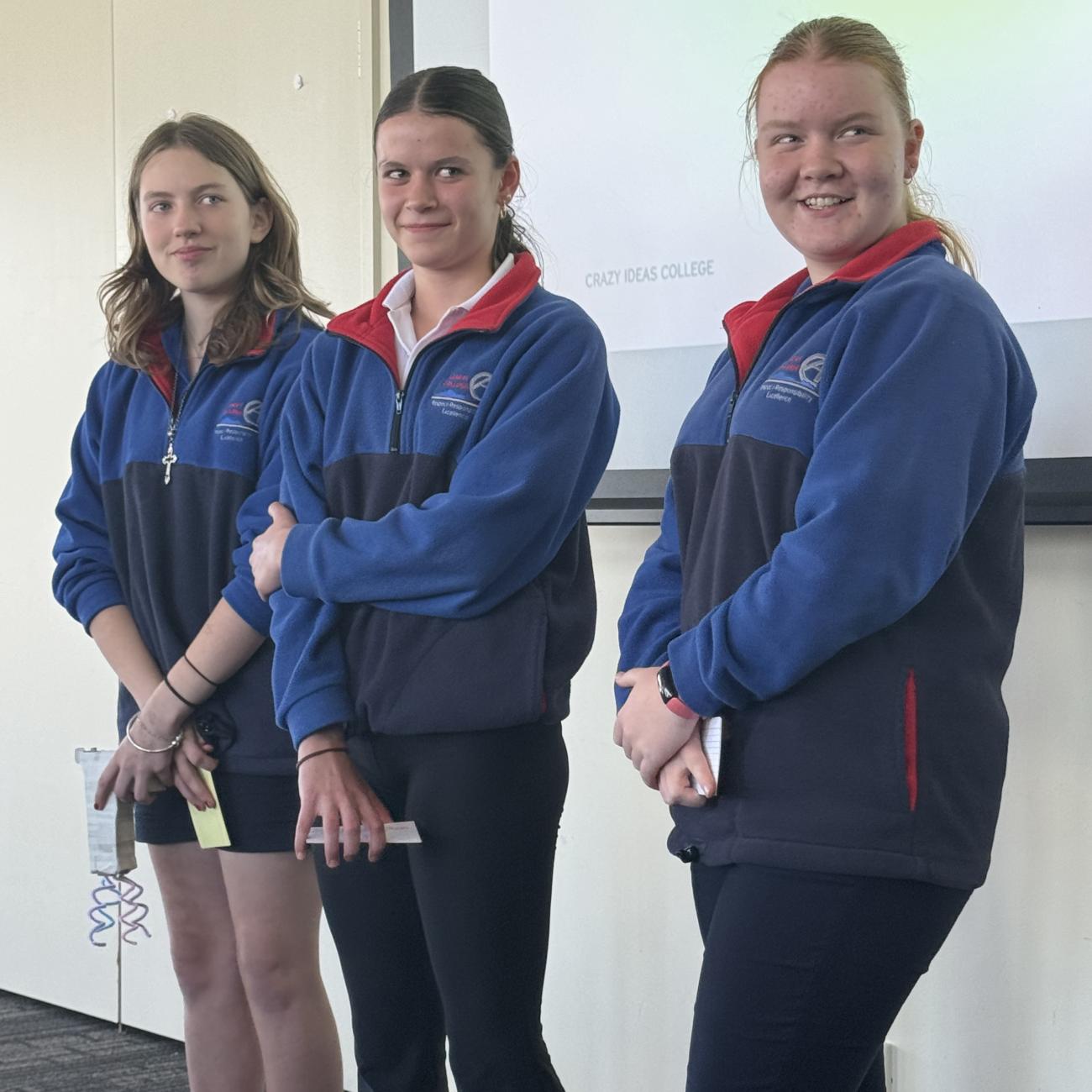 Three young women standing in front of an audience, smiling