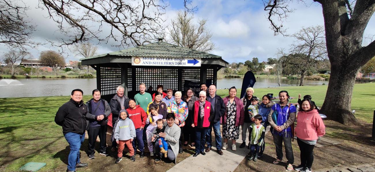 A group of 15 people standing outside on a sunny day in a botanical garden setting.