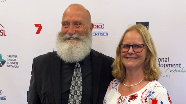 Man and woman standing in front of media wall and smiling