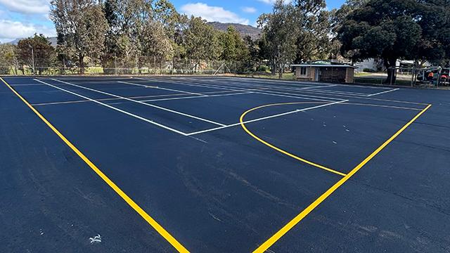 Freshly sealed tennis court with bright blue sky behind