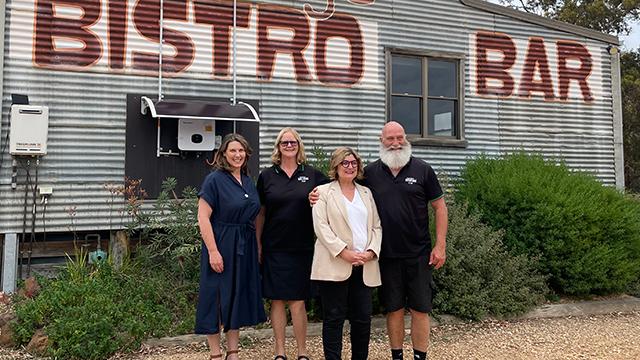 Four people standing together and smiling in front of a regional bar and bistro building